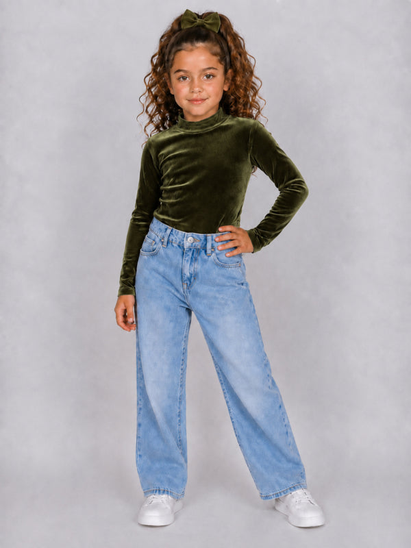 Meisje draagt armygroene velours coltrui met lange mouwen, gecombineerd met een lichtblauwe wide leg jeans en witte sneakers.